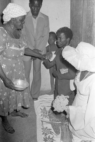 Woman standing in front of kneeling wedding couple, San Basilio del Palenque, ca. 1978