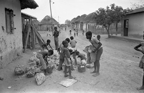 Small children pick up large boulders next to a building, San Basilio de Palenque, 1977