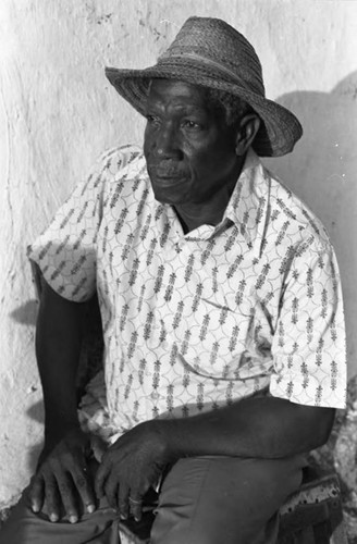 A man with a straw hat sits in front of a wall, San Basilio de Palenque, 1975