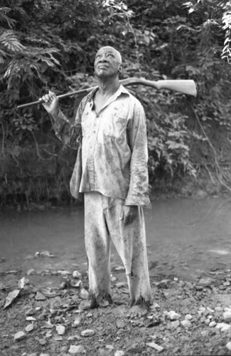 Fermín Herrera stands by the river with a rifle, San Basilio de Palenque, 1975