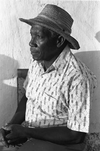 A man with a straw hat sits in front of a wall, San Basilio de Palenque, 1975