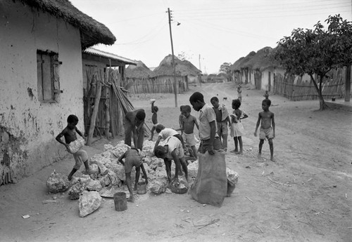 Small children pick up large boulders next to a building, San Basilio de Palenque, 1977