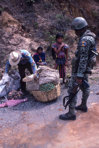 A soldier inspecting a Mayan man's basket in search of subversive materials, Chichicastenango, 1982