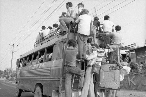 Civilians travelling through town on and in a city bus, San Salvador, circa 1980