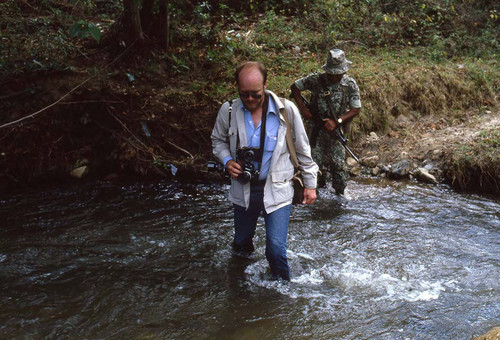 Photojournalist Steve Clevenger crossing a river with a soldier, Guatemala, 1982