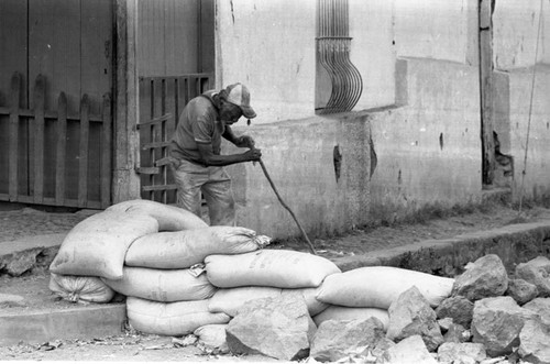 An old man inspects bags laying on the ground, Alegría, 1983