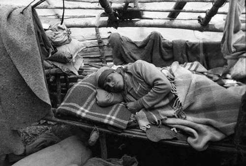 refugee man lays on a makeshift cot made of logs, Chiapas, 1983