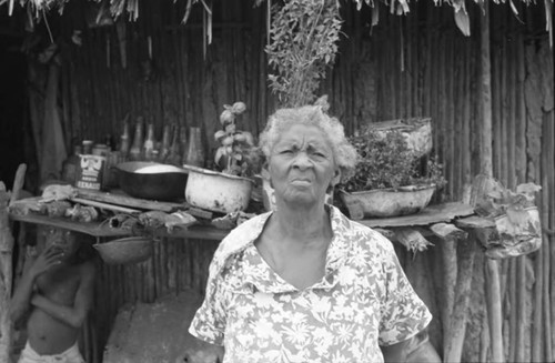 Woman stands in front of a wooden shelf, San Basilio de Palenque, 1975