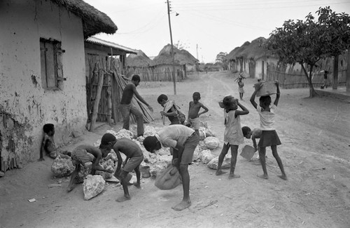 Small children pick up large boulders next to a building, San Basilio de Palenque, 1977