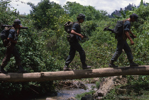 Three Contra soldiers cross a log bridge, Nicaragua, 1983