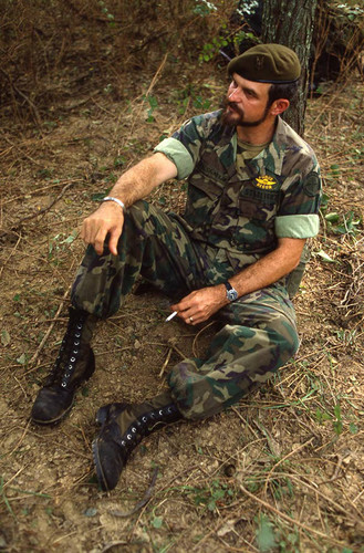 Survival camp instructor sits on grassfield, Liberal, 1982