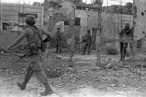 Army soldiers walk through ruins , Perquín, 1983