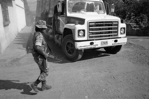 Armed soldier walks near a Coca-Cola truck, Guatemala, 1982