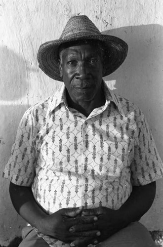 A man with a straw hat sits in front of a wall, San Basilio de Palenque, 1975