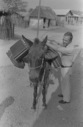 Man loading a mule with suitcases, San Basilio de Palenque, ca. 1978