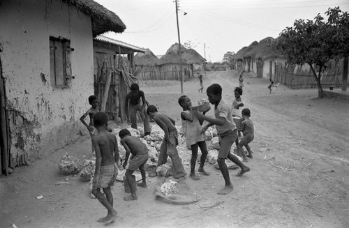 Small children pick up large boulders next to a building, San Basilio de Palenque, 1977