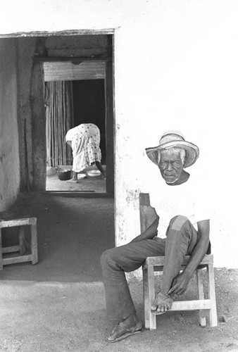 Man sits in front of a house, San Basilio de Palenque, 1975