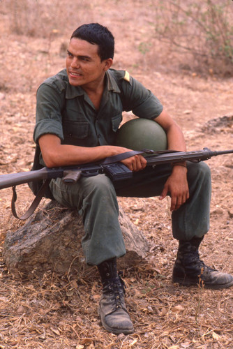 Soldier sitting with weapon on his legs, San Antonio de los Ranchos, Chalatenango, El Salvador, 1981