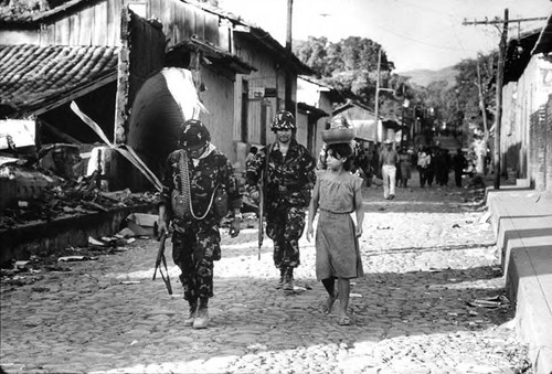 Girl walks beside two soldiers, San Agustín, Usulután, 1983