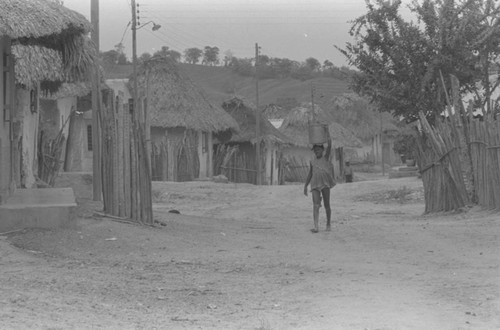 Girl walking with container on her head, San Basilio de Palenque, 1976