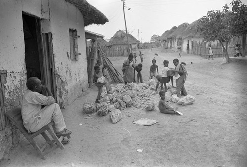 Small children pick up large boulders next to a building, San Basilio de Palenque, 1977