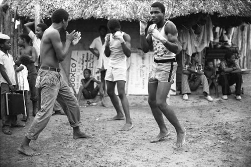 Three men boxing outdoor in front of a crowd, San Basilio de Palenque, 1975