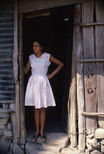 Woman standing outside marked home, Meanguera, Morazán , 1981