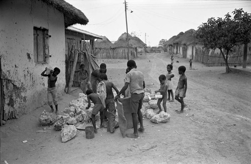 Small children pick up large boulders next to a building, San Basilio de Palenque, 1977