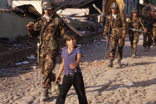 A young boy walks amongst soldiers, San Agustín, Usulután, 1983