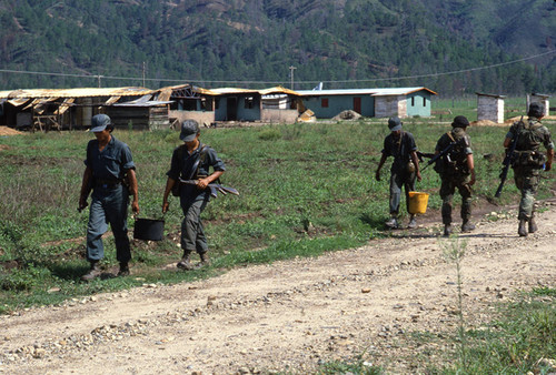 Contras carry containers down a road, Nicaragua, 1983