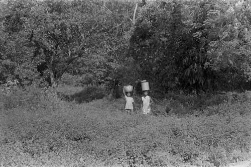 Two girls walking with a bucket on their head, San Basilio de Palenque, 1976
