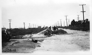 Looking west on the south roadway of Venice Boulevard from a point one block west of Sawtelle Boulevard showing storm water gushing from manhole, Los Angeles, 1928