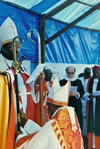 Fra bispevielsen af Nelson Kazoba i Lukajange, Karagwe Stift, Tanzania, 9. februar 1997. Stående til venstre: Biskop Samson Mushemba, som forestår indvielsen. I forgrunden: Biskop Nelson Kazoba. Bagved ses biskop Kresten Drejergaard, som medvirker ved skriftlæsningen