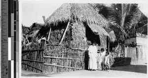 Sister M. Francisca Lucier, MM, standing with two children in front of a nipa hut, Malabon, Philippines, 1929