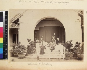 Missionary's daughter on horse outside house, India, ca. 1889