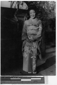 Smiling Japanese woman dressed in a kimono standing in front of a tree, Fushun, China, ca. 1937