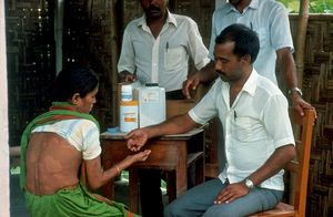 Diasserie, Bangladesh 1990: "Spedalskhed - den gamle svøbe" - Nr. 15: Kvinde der får medicin. Med den nye medicin, der er kommet indenfor de sidste 10 år, har man fået et effektivt våben i kampen mod den uhyggelige sygdom. Stadig tager behandlingen dog mindst 6 måneder for dem med høj modstandskraft, og mindst 24 måneder for patienter med lav eller ingen modstandskraft. Den moderne kombinations-behandling består af 3 midler, og er meget effektiv til at gøre patienter smittefri. I behandlingsarbejdet er den store udfordring nu at bruge midlerne ansvarsfuldt, så bacillerne ikke får mulighed for at udvikle resistens. Dermed har man nu en mulighed for at få sygdommen under kontrol, men stadig vil det kræve en stor indsats og tage et betragteligt antal år