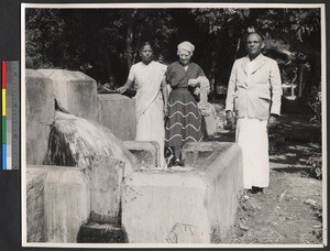 Elderly woman standing with two others by a flowing well, India, ca.1919-1943