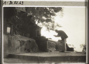 A chinese making prayers of petition in front of the altar of the great rock-king of the mountain of the spirits. (1929)