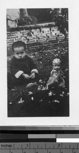 Orphan seated on the grass with doll, Loting, China, ca. 1930