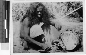 Man playing a drum to signal a death, Oceania, 1935