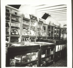 Hampanakatta shop in Mangalore, May 1938. Interior, seen from the left side. The cashier sits to the left of the first display case. The display cases have been newly made to give the shop a good and unified appearance