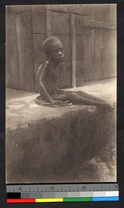 Emaciated child sitting by building, Gabon, ca.1935