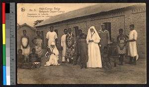 Missionary sister standing with others outside a tin-roofed brick building, Congo, ca.1920-1940