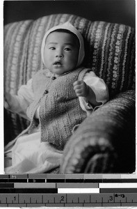 Japanese baby sitting in an upholstered chair, Japan, ca. 1948