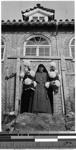 Maryknoll Sister Juliana posing with ornaments in front of Maryknoll convent, Gishu, Korea, 1925