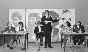 Landsstævnet 1972 i Holstebro. Landssekretær Simon Thorup er konferencier ved en "Quiz om DMS og andet". Fra venstre overlærer Marie Pihl, Rønne, Anette Andersen, Levring, fru Ester Fredborg, Asferg, og forstander Hald Nielsen, Holstebro. I baggrunden kontrollerer sognepræst Mogens Breiner Henriksen, medlem af bestyrelsen, at alt går korrekt til