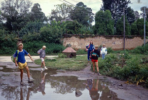 Den Norske Skole i Kathmandu, Nepal, 1991. Vi er på vej til skolens dansklokale, som ligger ca. 50 m fra hovedbygningen. Nu er det regntid, og vi skal passere en kæmpestor vandpyt!