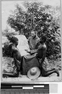 Priest explaining a photo to two boys, Sierra Leone, Africa, ca. 1920-1940