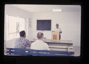 man standing behind a pulpit inside a church building or classroom